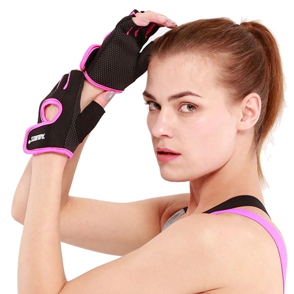 Black half-finger gym gloves with pink trim and looped wrist strap; person holds one glove up